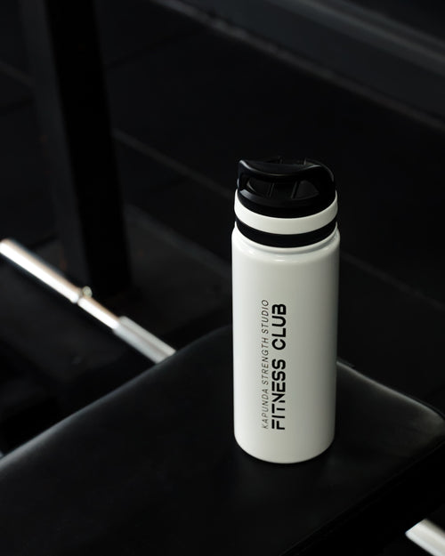 A white insulated water bottle with a black lid, featuring the vertical text 'JERSEYSWEATENESS STUDIO FITNESS CLUB', resting on a black gym bench.