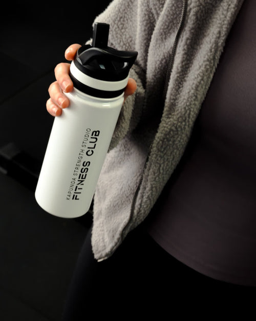 A person in a gym holding a white insulated water bottle with a black lid. The bottle has the text 'FITNESS CLUB' printed vertically on the side.