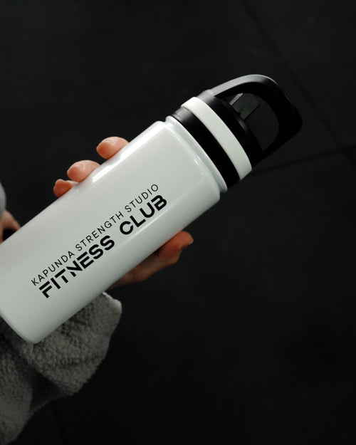A person in a gray fleece jacket holds a white insulated water bottle with a black lid. The bottle is printed with the text 'KARUNISTRENGTHSTUDIO FITNESS CLUB'.